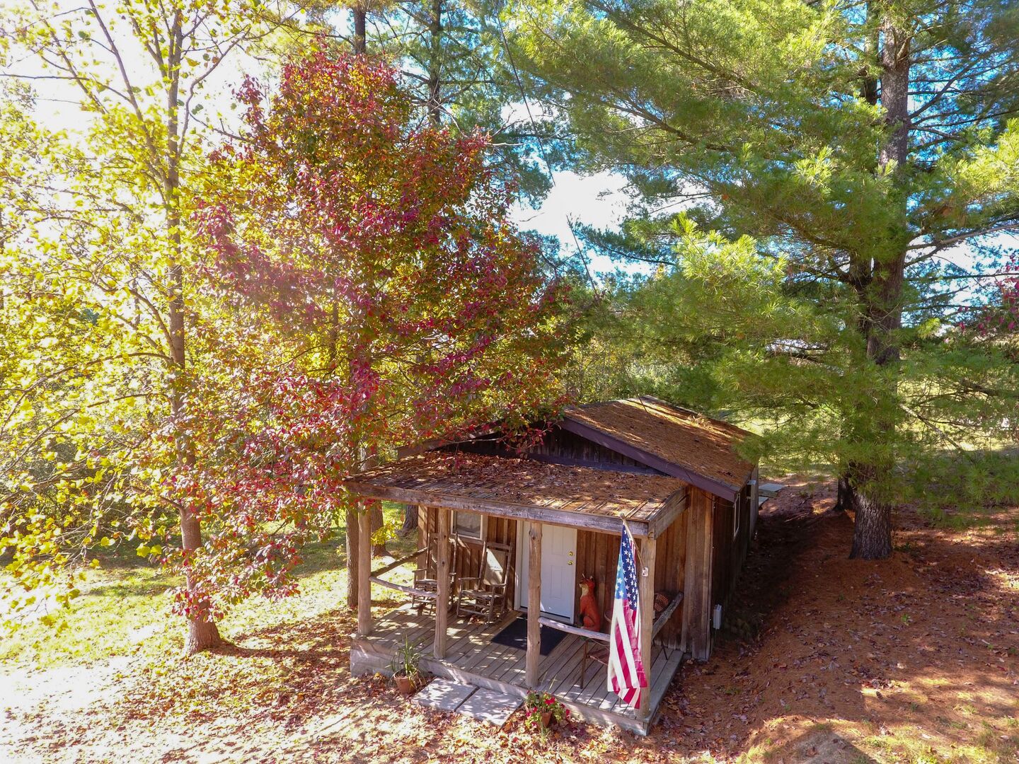 A rustic wooden cabin with a porch, surrounded by trees and a flag.
