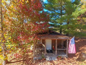 A rustic cabin with a porch, surrounded by autumn foliage.