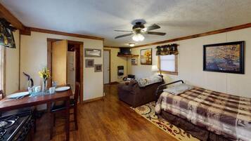 A compact room with a kitchenette, a sofa, a bed, and a ceiling fan.