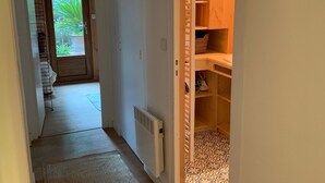 A narrow hallway with a wooden door leading to a room with a patterned floor and shelves. A radiator is visible on the wall, and a light fixture hangs from the ceiling. - Wooden house in the center of Cap Ferrets ans a quiet street 100 m from the market. (Lège-Cap-Ferret)