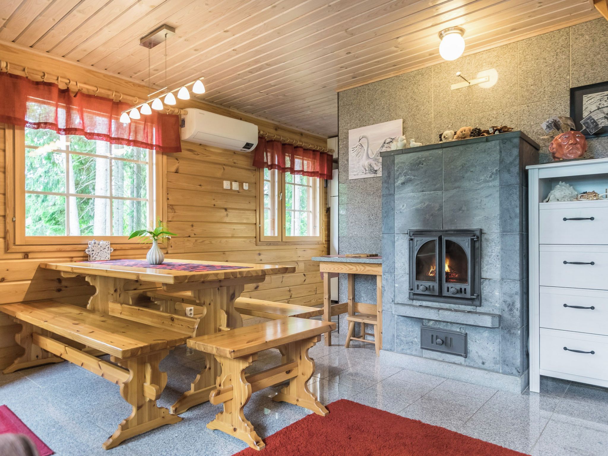 Un interior de madera con chimenea de piedra, bancos de madera y una mesa con un florero.