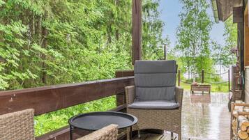 A covered outdoor seating area with wicker furniture and a table, surrounded by lush greenery.
