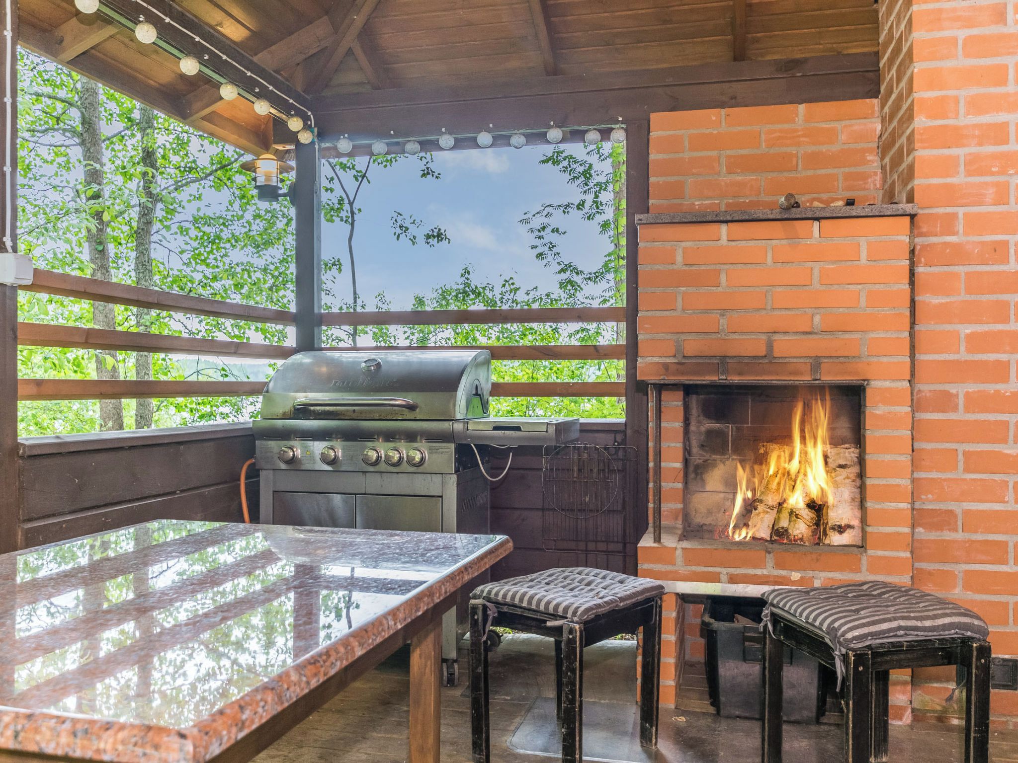 An outdoor barbecue area with a grill, a brick fireplace, and a table with chairs.