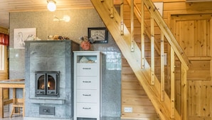 A cozy room with a stone fireplace, a wooden staircase, and a white cabinet with drawers.