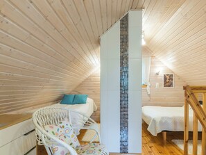 A cozy room with a bed, a white chair with a colorful cushion, a small table, and a vertical glass partition. - Joutsen by Interhome (Ruovesi)