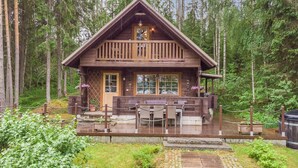 A wooden cabin with a balcony, surrounded by a forest.