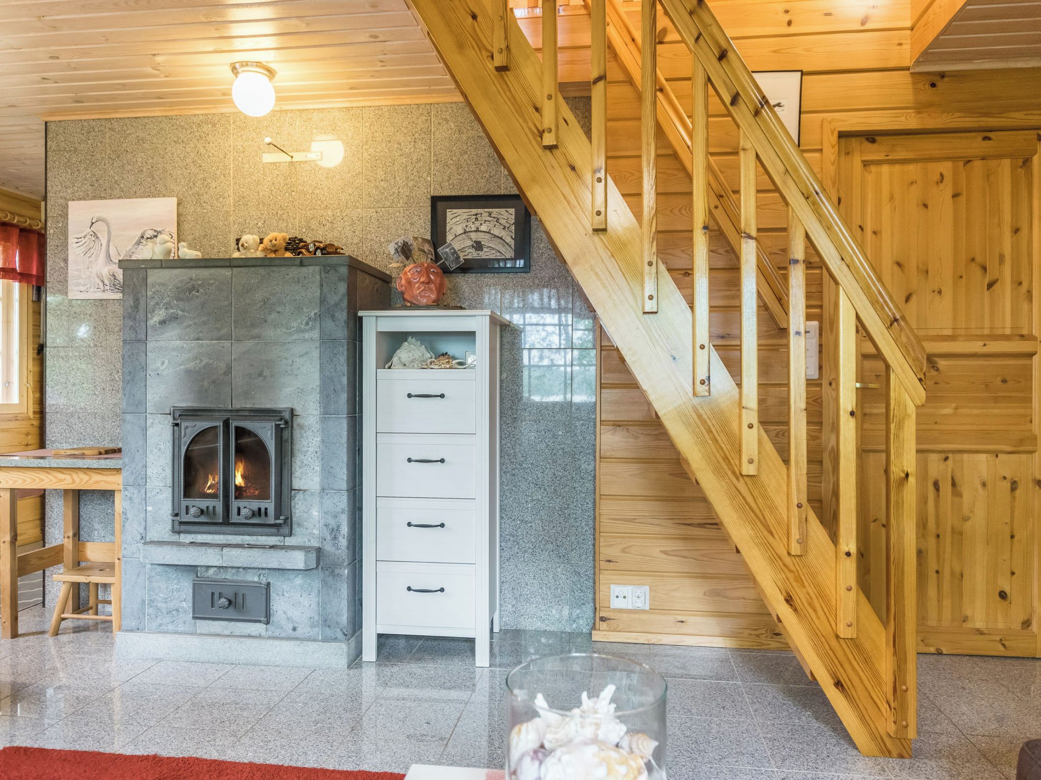 A cozy interior with a stone fireplace, wooden staircase, and a white cabinet.