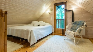 A cozy attic bedroom with a bed, a rocking chair, and a view of the outdoors through a door.
