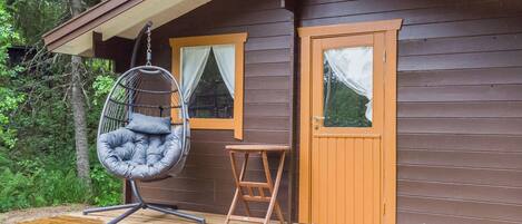 Een houten chalet met een veranda, een hangstoel, een kleine tafel en een deur.