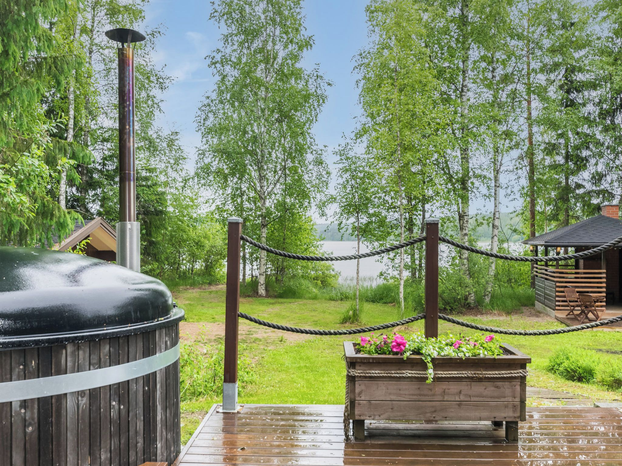Eine Holzterrasse mit Whirlpool, einer Seilsperre und einer Holzhütte in einem bewaldeten Gebiet.