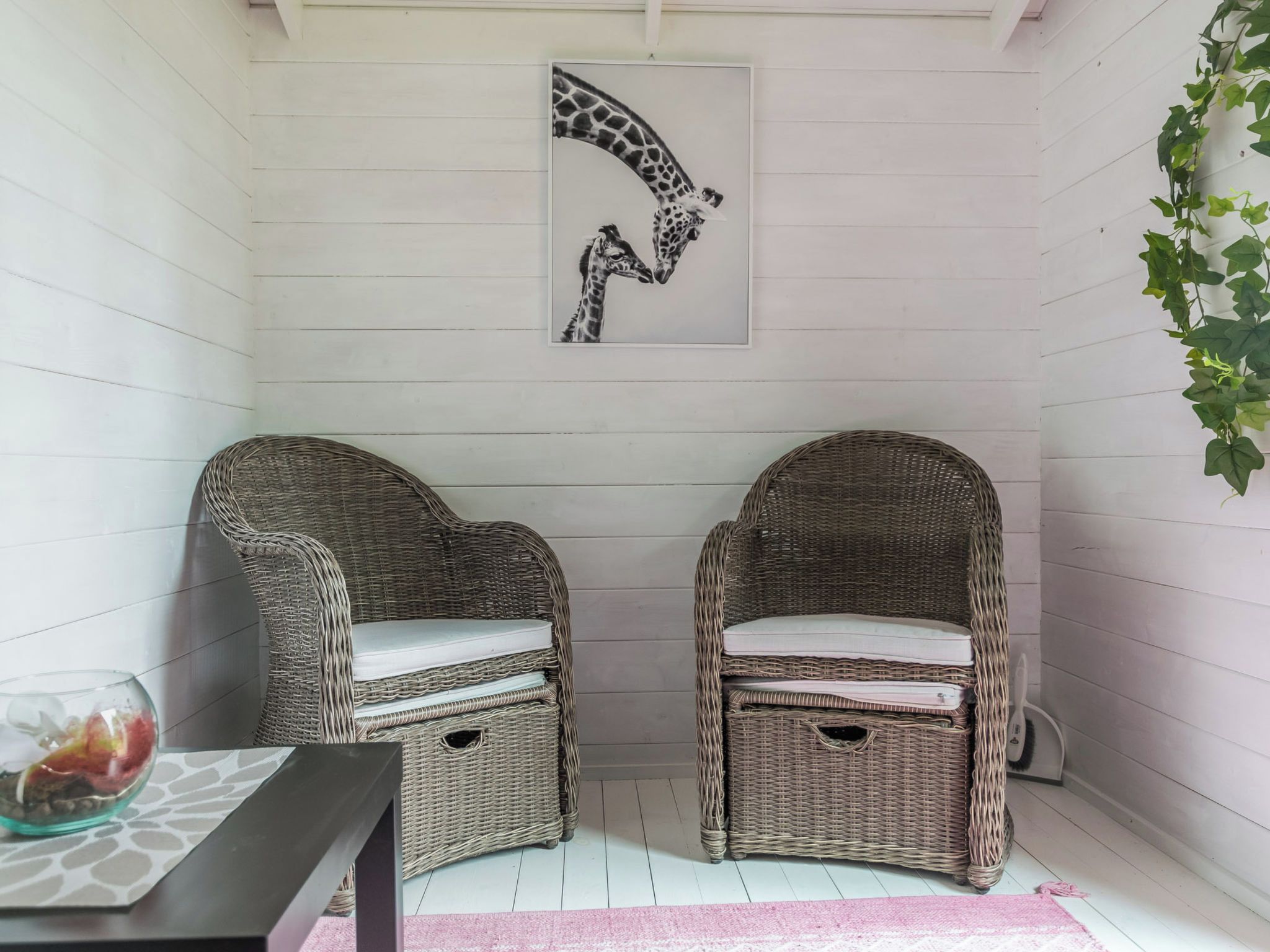 A room with two wicker chairs, a white wall, and a framed giraffe artwork.