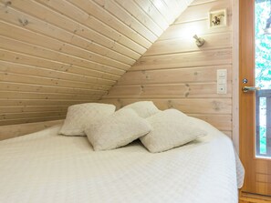 A bedroom with a sloped ceiling, wooden walls, a bed with white bedding, and a door with a window. - Joutsen by Interhome (Ruovesi)