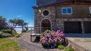 A two-story house with a stone facade, a wooden deck, and a view of the ocean. - Ocean Front Hot Tub, South Beach, Newport, Dog Friendly! (South Beach)