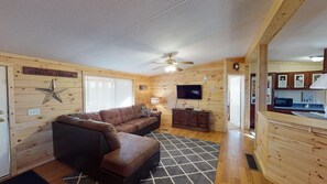 A cozy cabin-style room with a brown leather sofa, a television, and a ceiling fan.