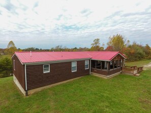 A log cabin with a red roof, a porch, and a grassy yard.