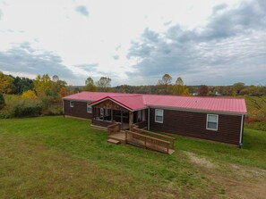 A two-story log cabin with a red metal roof, a porch, and a small deck.