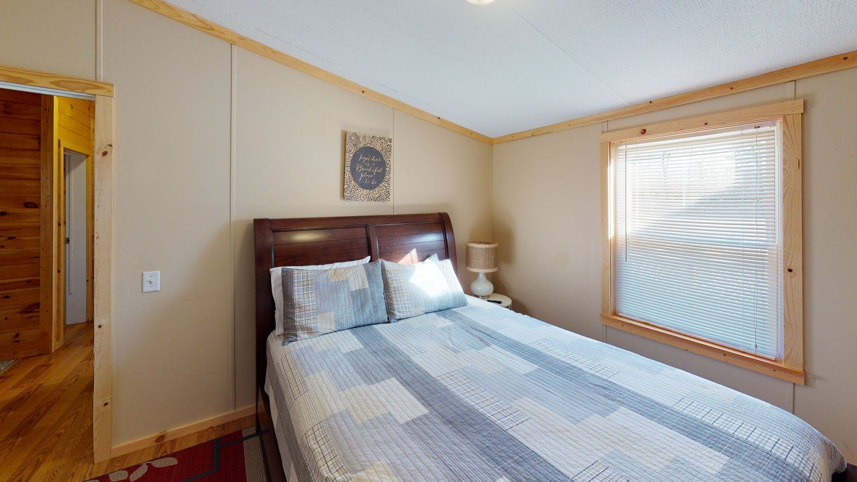 Un dormitorio con cabecera de madera, cama con colcha estampada, lámpara de noche y ventana con persianas.