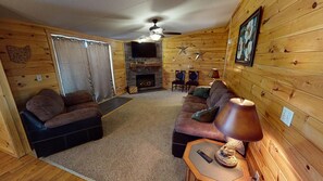 A cozy log cabin interior with a fireplace, a ceiling fan, and a television.