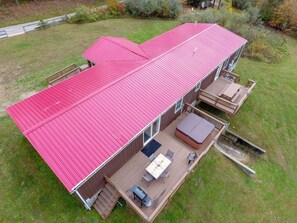 A two-story house with a red metal roof, a deck with outdoor furniture, and a hot tub.