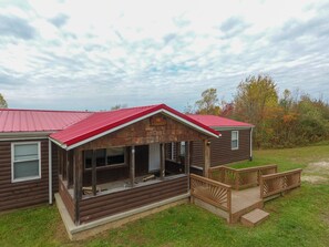 A rustic cabin with a red roof, a porch with wooden railings, and a small deck.