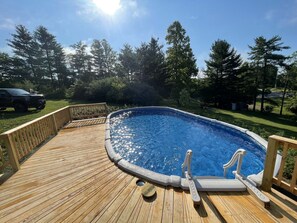 A wooden deck surrounding a swimming pool with a diving board and steps.