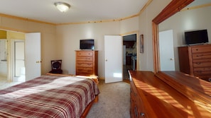 A bedroom with a bed, dresser, mirror, and a television on a stand.