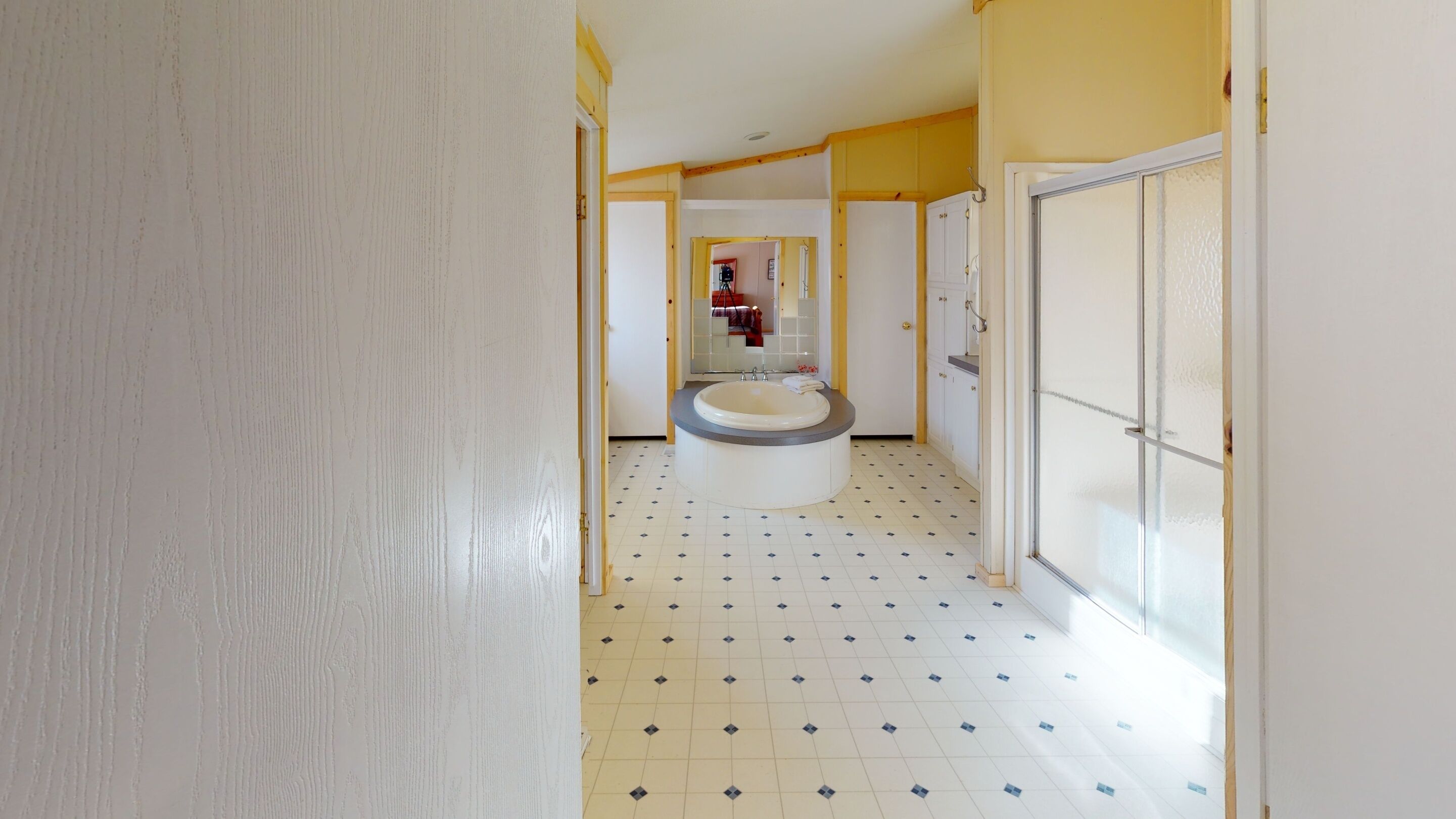 Un pasillo con una bañera, suelo de baldosas y una puerta que da a un cuarto con un espejo.