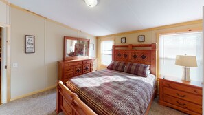 A bedroom with a wooden bed, a dresser, a mirror, and a window with blinds.