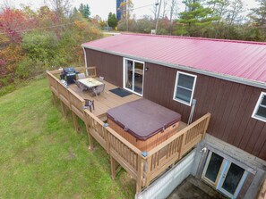 A wooden deck with a hot tub, a barbecue, and a table with chairs.
