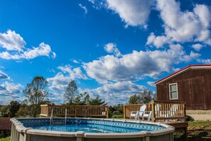 A backyard with a swimming pool, wooden deck, and a house.