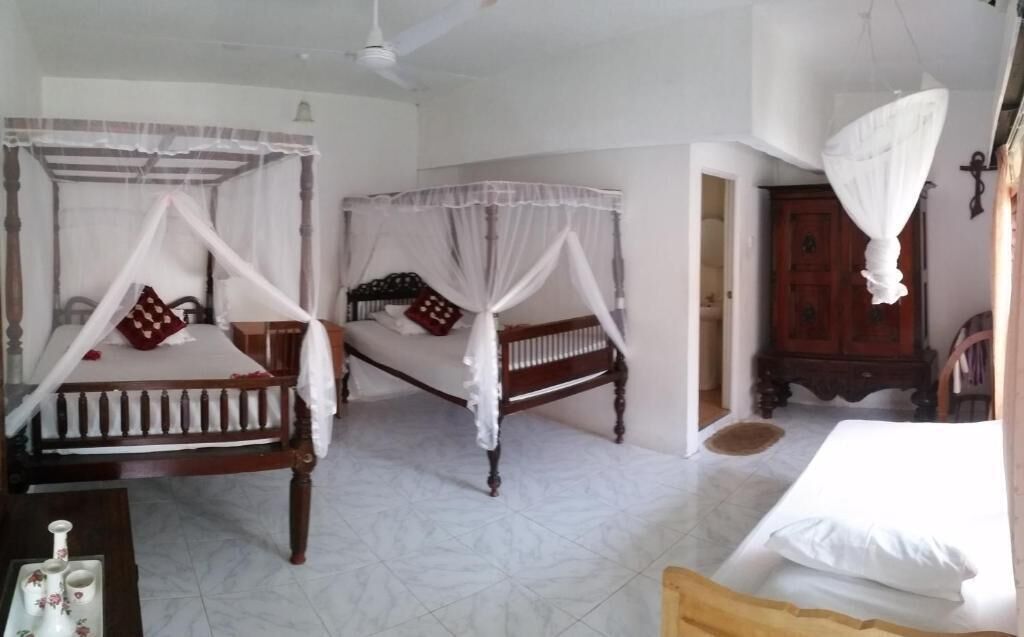 A room with two wooden beds, each with a canopy, a wooden cabinet, and a white tiled floor.