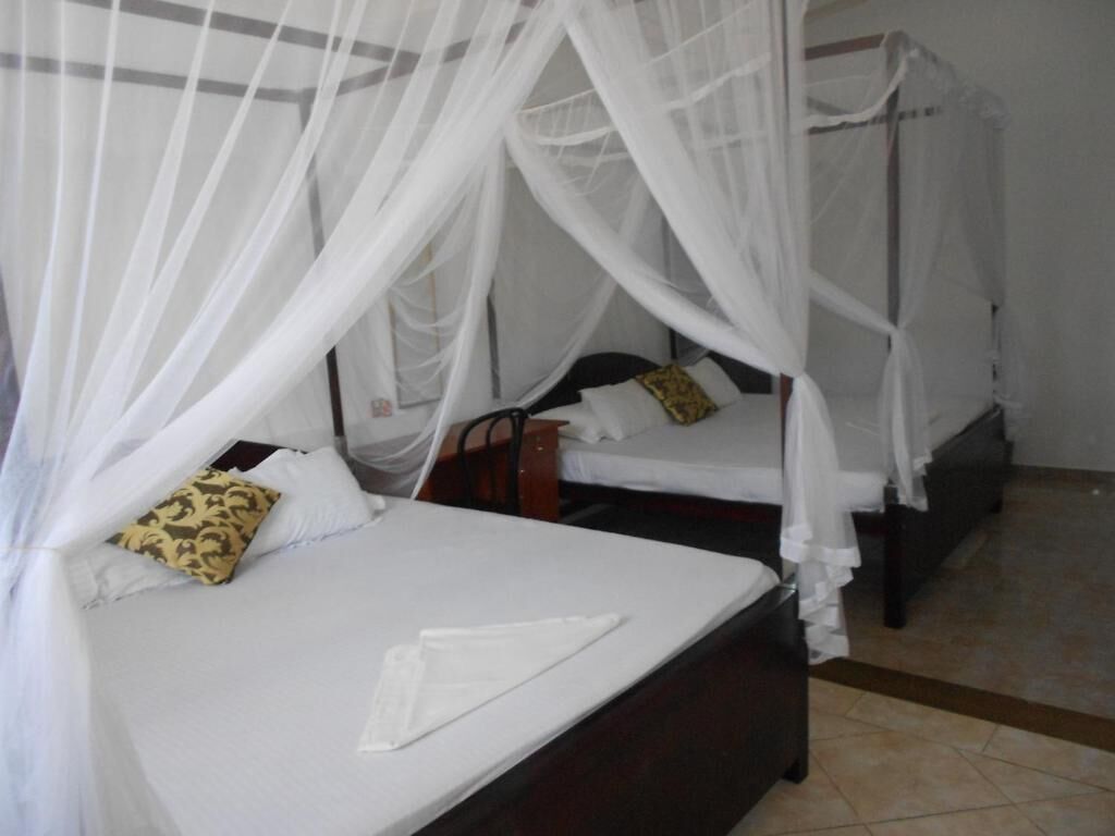 Une chambre avec deux lits, chacun doté d’un baldaquin. Les lits sont garnis de draps blancs et possèdent une tête de lit en bois.