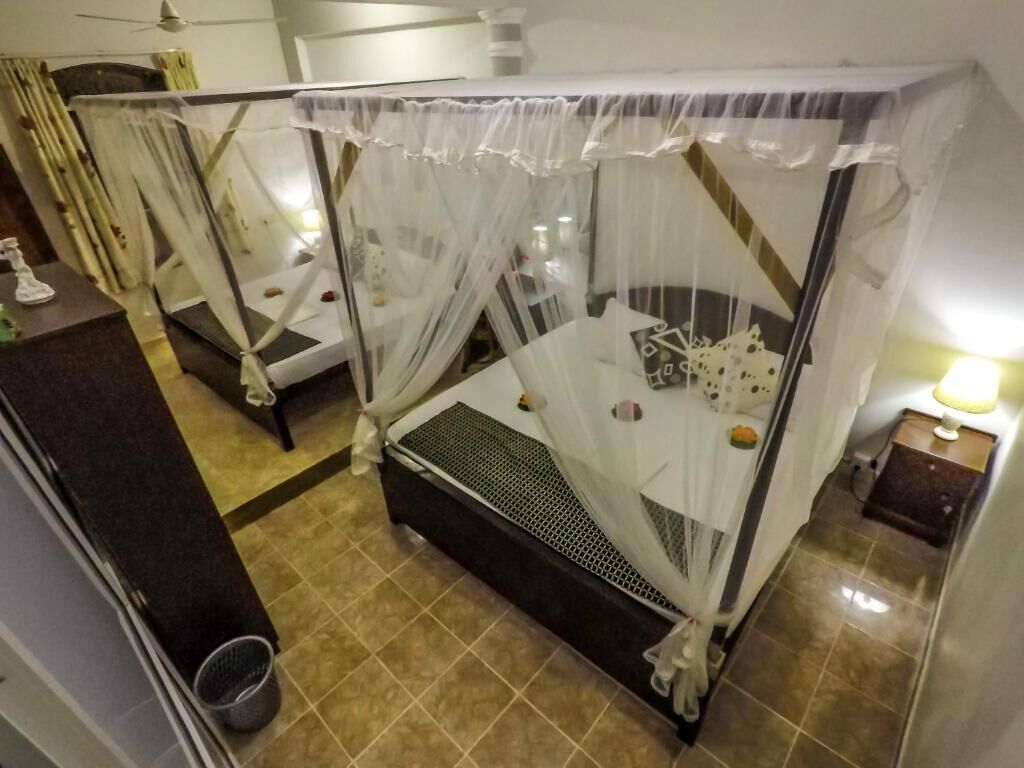 A hotel room with a bed covered by a white canopy, a small bedside table with a lamp, and a trash bin.