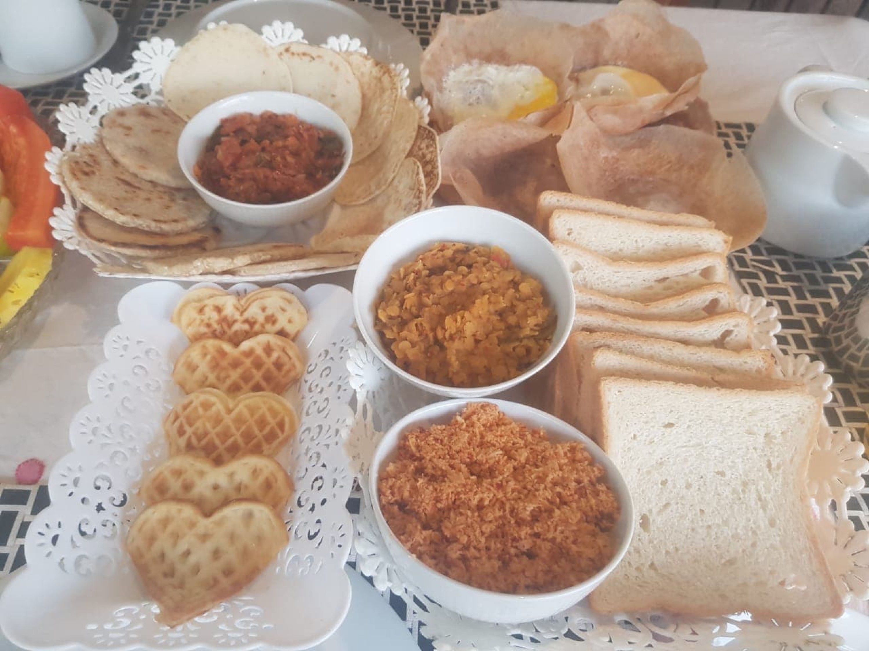 Une table où sont disposés divers aliments, notamment du pain, des gaufres et des bols contenant différentes sauces et condiments.