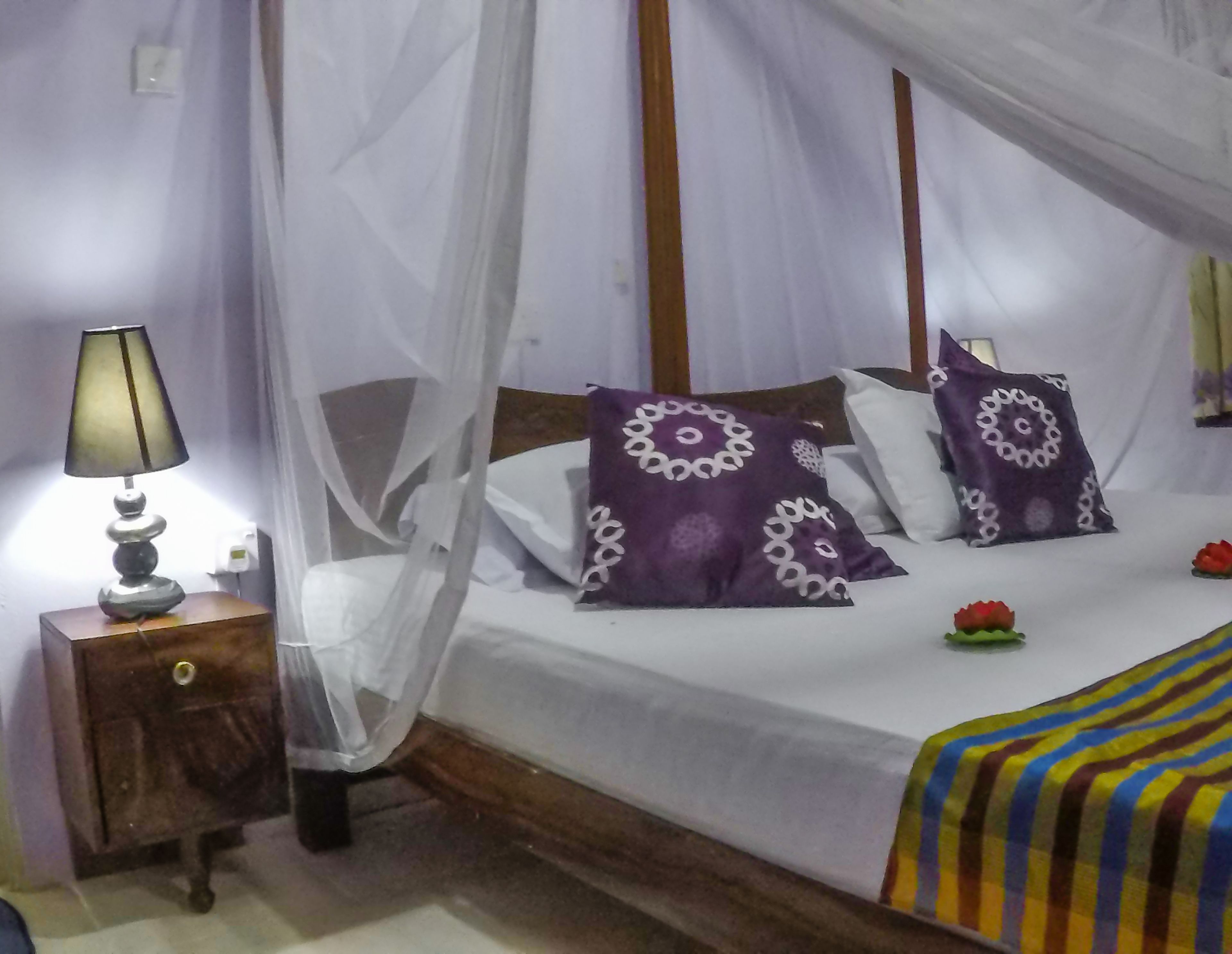 A bed with a canopy, two pillows with a circular pattern, a bedside lamp, and a striped blanket.