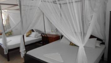 A room with two beds, each covered with white sheets and a canopy.