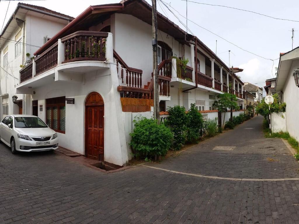 A residential street with white houses, a parked car, and a cobblestone road.