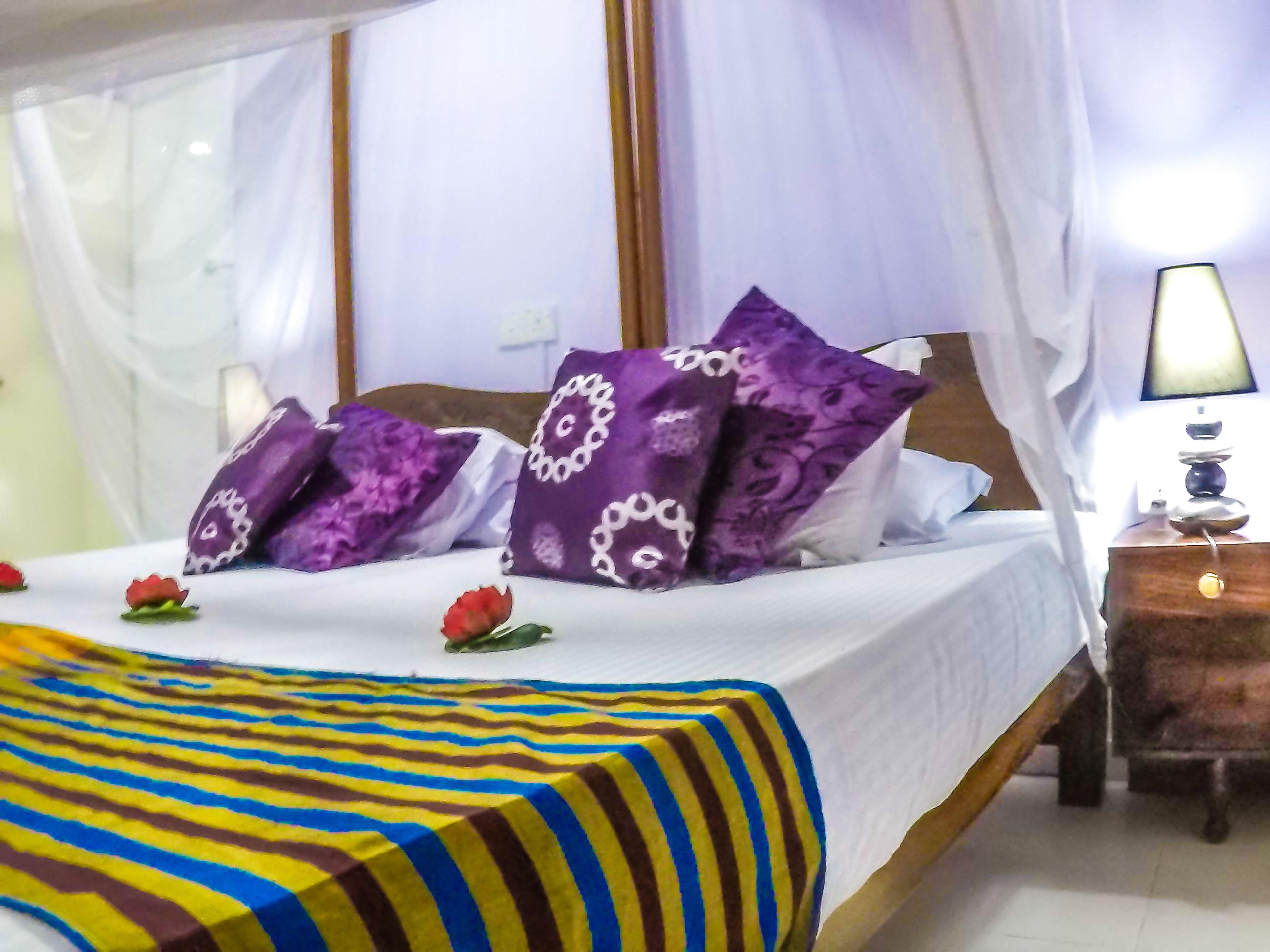 Una cama con colcha a rayas, almohadas moradas y un dosel blanco.