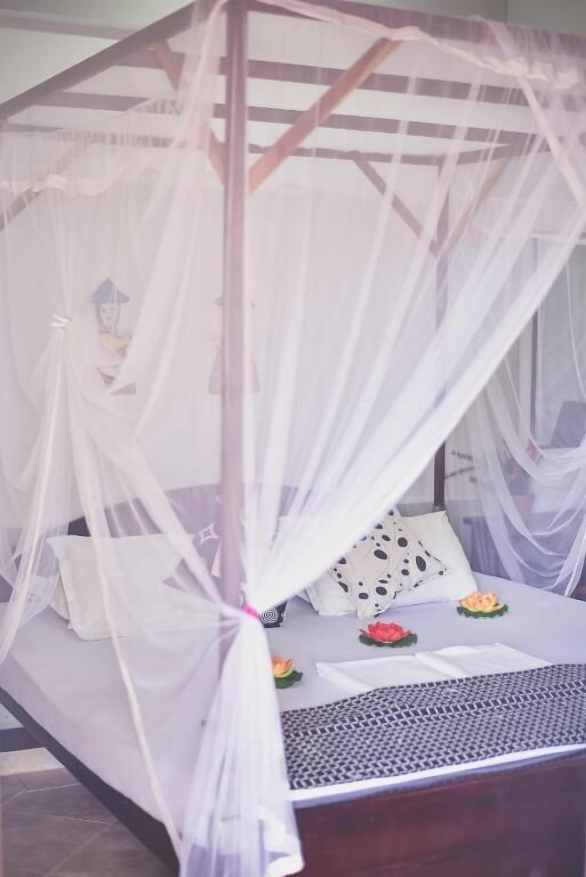 A bed with a canopy, pillows, and a small table with a book and a flower.