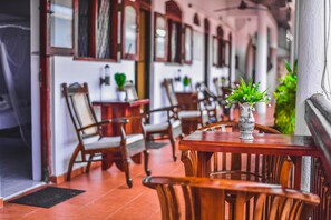 Un restaurant avec des tables et des chaises en bois, un vase avec une plante sur l’une des tables, et une porte avec un paillasson.