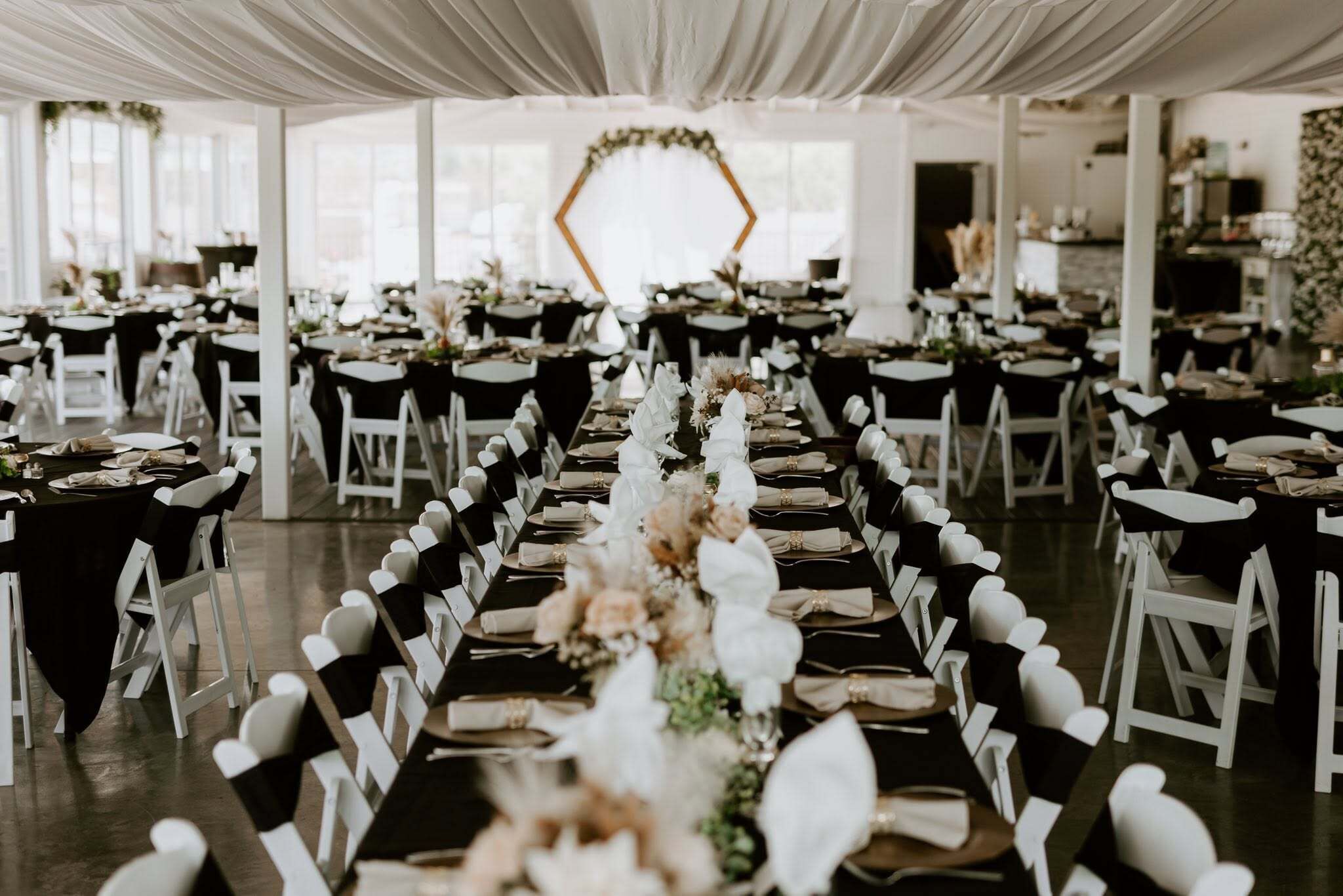 A banquet hall with rows of tables, white chairs, and a central aisle.