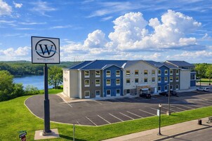 A hotel with a parking lot, a sign with a logo, and a lake in the background.