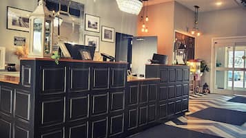 A reception desk with a black panel design, a chandelier, framed pictures on the wall, and a patterned floor.