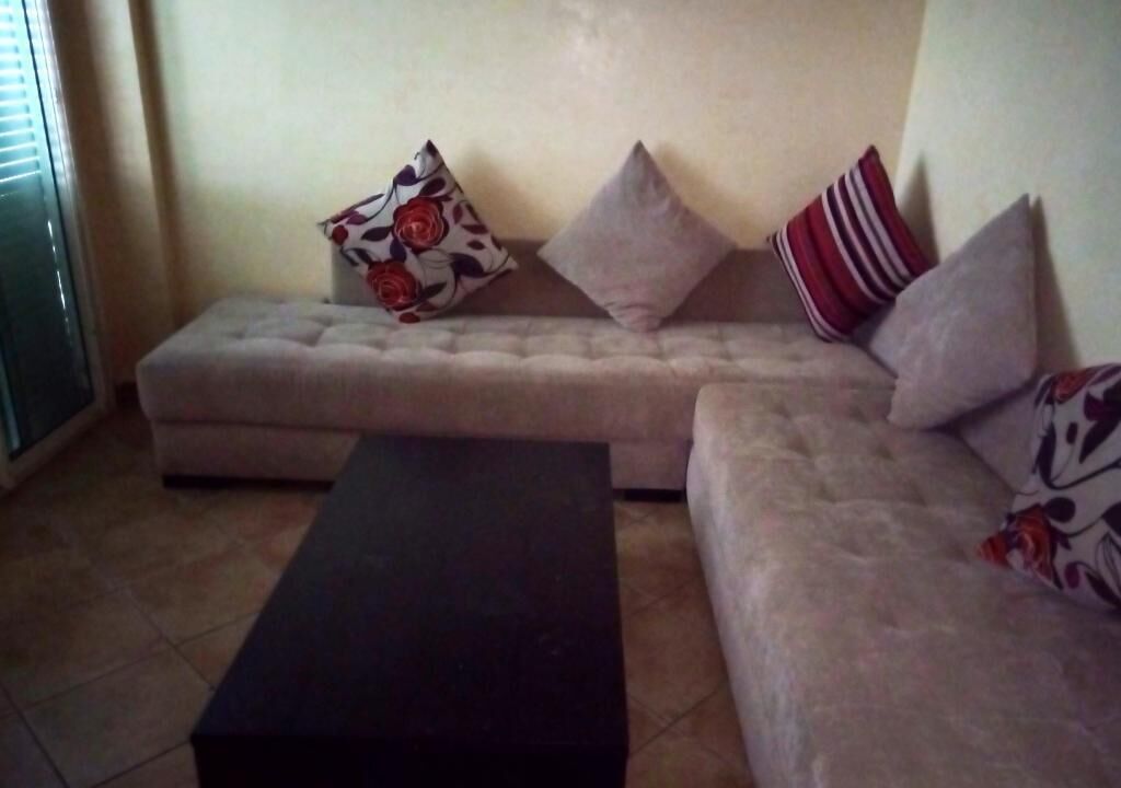 A living room with a sofa set, a black ottoman, and patterned cushions.