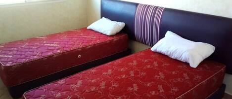 Deux matelas rouges avec des oreillers blancs dans une pièce dont le mur est uni et qui possède une fenêtre.