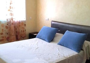 A bed with white bedding and two blue pillows, a dark headboard, and a nightstand with a lamp. - Residence Riviera Beach 4111 (Cabo Negro)