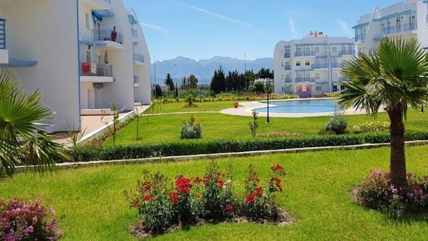 A modern hotel with a pool, well-maintained gardens, and a clear view of mountains in the background. - Residence Riviera Beach 4112 (Cabo Negro)
