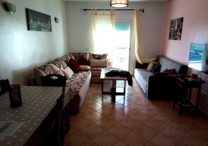 A living room with a sofa, a coffee table, a TV, and a dining table.