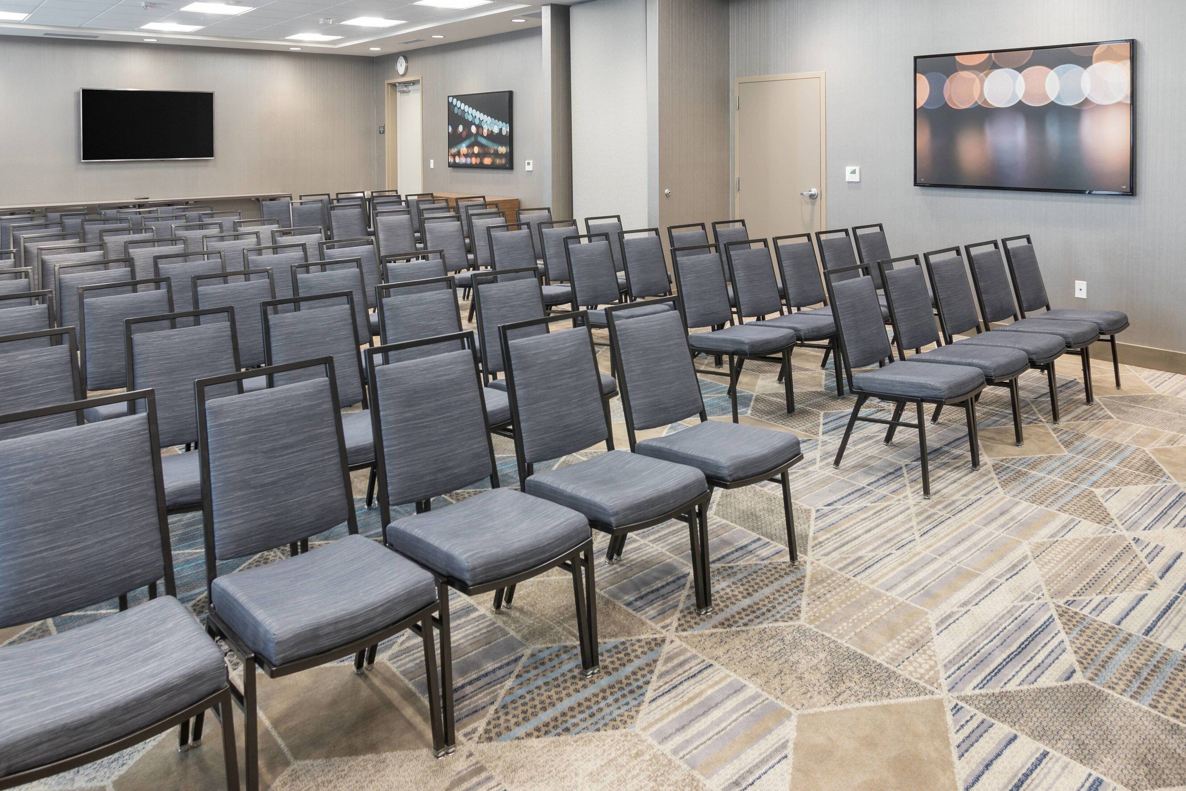 A conference room with rows of grey chairs, a large screen, and a patterned carpet.