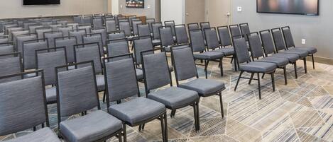 A conference room with rows of grey chairs, a large screen, and a patterned carpet.